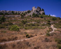 Ruins of Chateau Perillos east of Tuchan situated on hillside with scattered outcrops of rock and windswept vegetation and narrow  stony track in foreground.