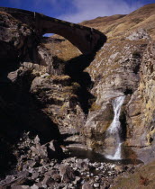 Defile de Tourmont.  Gave de Brousset waterfall flowing from rocks into pool below with arched bridge above.