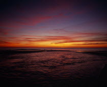 Cap de L Homy.  Red and orange sunset sky over Atlantic coastline with windswept clouds and rippled water surface.