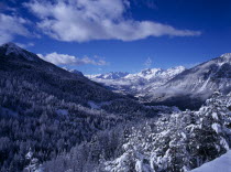 View west from Col de Montgenevre over snow covered trees towards Ecrin National Peak and mountain peaks.