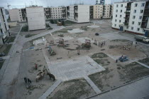 Multi storey housing in coal mining town surrounding playground with children playing and horses tied to street light and swing frame.