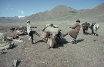 Two men preparing to leave camp  loading pack camel and pulling ropes tight.