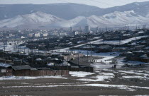 Traditional housing surrounding Soviet built city centre in winter snow with mountain backdrop.