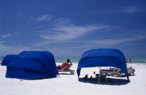 Blue wind breaks and sunbathers on sandy beach