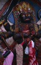 Women making offerings at the Kala Bhairab or black Shiva in Durbar Square representing the fearsome Tantric form of Shiva in Nepal.