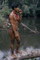 Barasana headman Bosco stands on log at river port smoking home grown tobacco  body painted dark purple with we leaf dye decoration Tukano sedentary Indian tribe North Western Amazonia body decoration...