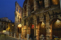 Piazza Bra.  Arena Roman amphitheatre completed in AD 30.  Part view of exterior at night with bicycles chained against railings in foreground and blur of passing traffic.