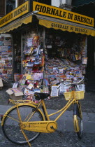 Piazza della Loggia.  Newspaper stand with yellow painted bicycle advertising name.