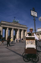 Brandenburg Gate. Man in foreground under Pariser Platz sign performing with a Orgelbau Stuber Organ and a puppet monkey