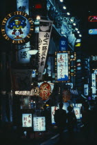 City street scene at night with illuminated neon signs advertising bars  restaurants and other entertainments.  Couple walking in picture centre.