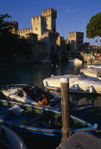 Sirmione.  Rocca Scaligera medieval castle with crowds of visitors crossing bridge to entrance.  Moored boats in foreground.