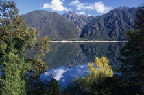 Lago d Iseo.  Trees and mountain landscape reflected in still surface of lake.