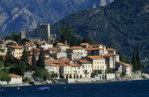 Rezzonico.  View across lake to red tiled rooftops of village houses with castle tower and walls behind.