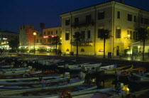 Bardolino.  Harbour and moored boats at night with waterside bars and hotels and illuminated street lights and signs.