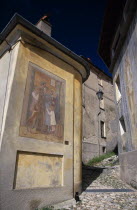 Narrow cobbled street with fresco decoration on exterior wall of corner building.