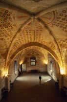 Angera.  Interior of reception hall in Rocca di Angera medieval castle with painted vaulted ceiling and fresco wall decoration.  Female visitor looking up at paintings.