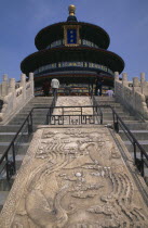 Tiantan Park.  Stone walkway and view up steps towards the Hall of Prayer for Good Harvests with visitors looking at tiered and decorated exterior.