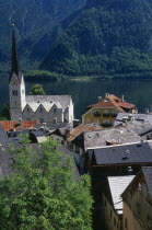 View over tiled village rooftops  hotel and church with Hallstattersee Lake and steep mountain backdrop.