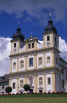 Maria Plain church of pilgrimage.  Baroque exterior facade with double tower and statues of the four evangelists and the Virgin and Child above the entrance.