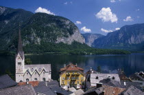 View over tiled village rooftops  hotel and church with lake and mountains behind.