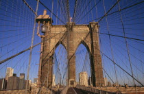 Brooklyn Bridge.  View across bridge towards Manhattan skyline part framed by central stone tower and intersected by steel wires and suspension cables.Spans the East River.  Construction began in 18...