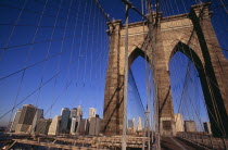 Brooklyn Bridge.  View across bridge towards Manhattan skyline part framed by stone tower and intersected by steel wires and suspension cables.Spans the East River.  Construction began in 1870 and t...