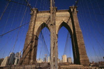 Brooklyn Bridge.  View along bridge to Manhattan skyline beyond part framed by central stone tower and intersected by steel wires and suspension cables.Spans the East River.  Construction began in 1...