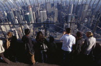 View north over city  from top of the Empire State Building at 8.30 a.m. with line of visitors looking out through expanse of glass.