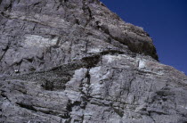 Kirghiz people leading pack horses along steep  narrow path high on rock face.