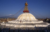 People circumambulate giant central stupa hung with prayer flags and painted with eyes of Buddha.  Town spread out beyond.