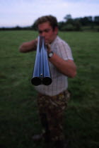 Man holding double barrelled shotgun with detail of the tip of the gun in focus.