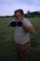 Man holding double barrelled shotgun with detail of the tip of the gun in focus.