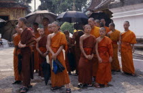 Group of young  Buddhist monks  some holding umbrellas as sun shades.