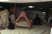 Bedouin desert encampment.  Woman and children inside tent with baby in traditional cradle