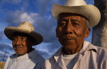 Two smiling  elderly men in hats  head and shoulders portraits one slightly behind other.