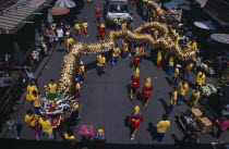 Chinese New Year.  View looking down on Dragon Dance and watching crowds under striped awning and sun umbrellas lining road.