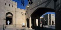 Town centre with crenellated walls and archway over quiet street.  Man framed by arched entrance in wall.