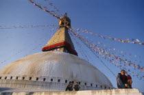 Part view of stupa hung with prayer flags and pilgrims.