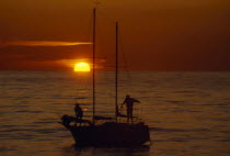 Two people seen on a sailing boat at sunset with red sky and a low sun. Borth  Wales  UK