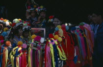 Akha girls wearing brightly coloured head-dresses gathered around tourists.