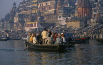 Tourists in boat being rowed passed the ghats on the River Ganges.Asia Bharat Holidaymakers Inde Indian Intiya Tourism