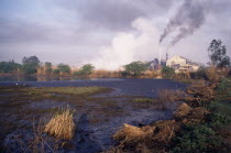 Sugar mill emitting dark clouds of smoke from chimneys beside polluted lake.air pollution  Asia Asian Bharat Ecology Entorno Environmental Environnement Farming Agraian Agricultural Growing Husbandry...