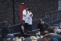 View over tightly packed sheep in a pens toward auctioneer at the weekly sheep fair