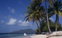 Sandy Island.  Tourists on sandy beach beneath palm trees with sailing ship moored in water beyond.Dependency of Grenada Beaches Caribbean Grenadian Greneda Holidaymakers Resort Scenic Seaside Shore...