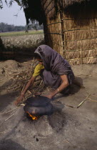 Woman cooking on small open fire with cooking pot held on raised clay surround.Asia Asian Bangladeshi Female Women Girl Lady One individual Solo Lone Solitary 1 Female Woman Girl Lady Single unitary