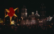 Crowds gathered in the Plaza de la Constitucion or Zocalo at Christmas with illuminated decorations at night.American Hispanic Latin America Latino Mexican Nite Xmas