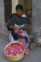 Woman flower seller sitting on step in street threading pink flower heads into garland.American Female Women Girl Lady Hispanic Kids Latin America Latino Mexican Religion Religious Female Woman Girl...