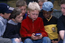 Boy playing with his Gameboy computer game whilst being watched by his friends