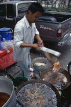 Thanon Silom male vendor at his stall on the pavement deep frying fish in woksAsian Prathet Thai Raja Anachakra Thai Siam Southeast Asia Siamese