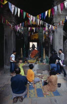 Banteay Kdei.  Cambodian visitors lighting incense at shrine with seated Buddha figure hung with coloured flags for Chinese New Year. Colored Asian Kampuchea Religion Southeast Asia History Kamphuche...